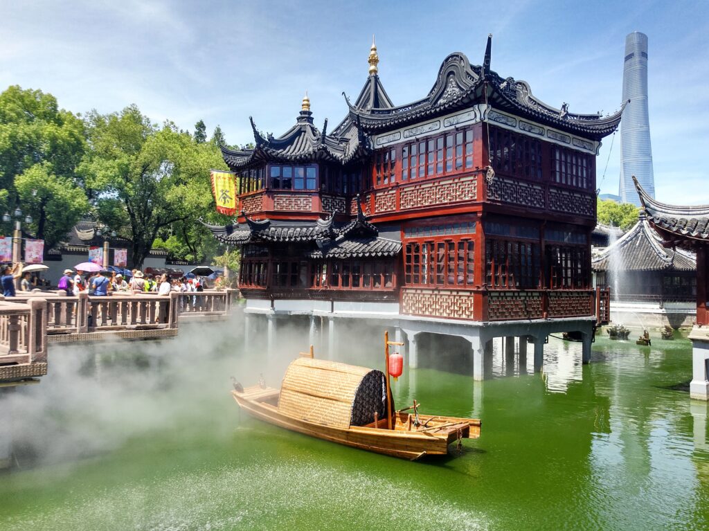 Casa de té tradicional china sobre el agua con un bote de madera en primer plano y un rascacielo moderno al fondo en Shanghai.