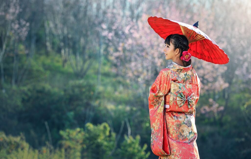 mujer vestida con un kimono tradicional y sosteniendo una sombrilla roja en un paisaje natural en Japón
